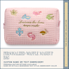 Pink waffle makeup bag with embroidered designs and text on a white background